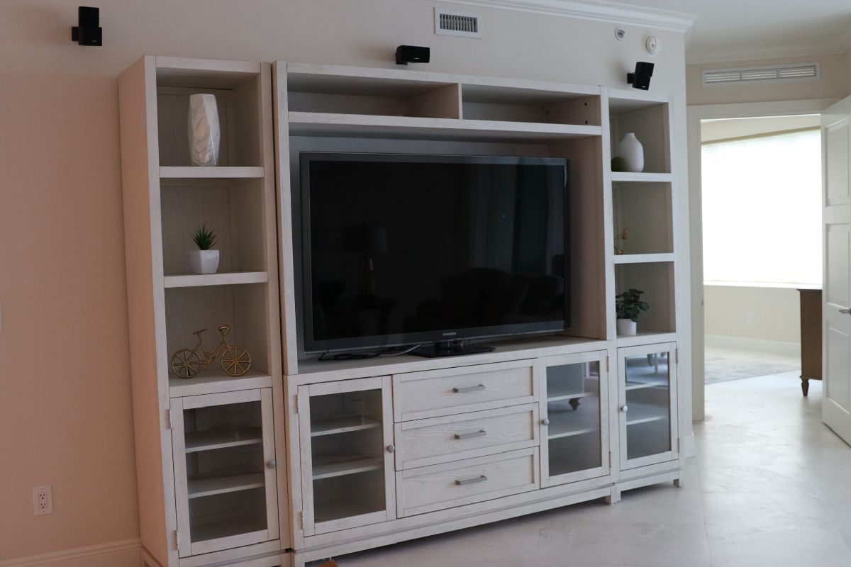 White built-in entertainment center with TV, shelves, cabinets, and speakers.