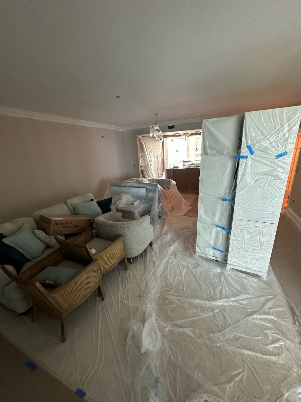Room with furniture covered in plastic sheeting. White wrapped panels and a couch are visible.