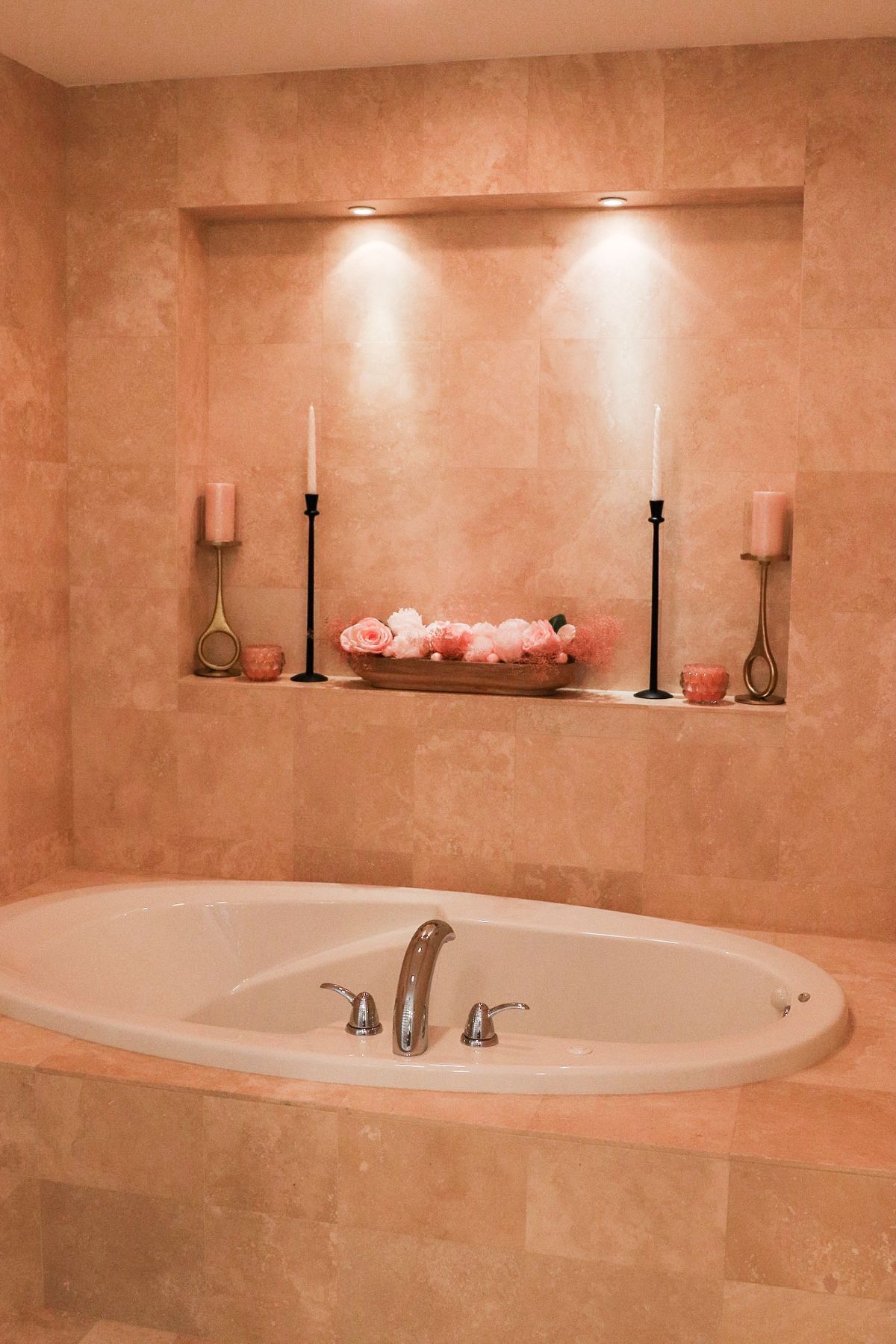 Bathroom with a built-in oval tub. A shelf above the tub holds candles and a bowl of flowers, lit by recessed lights.