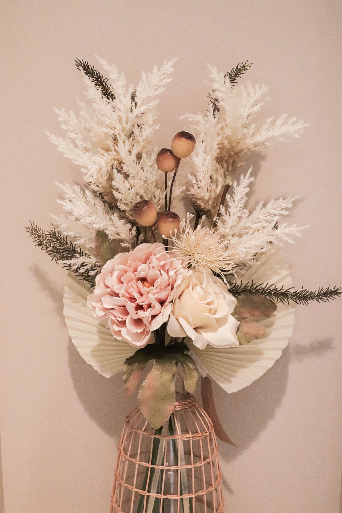 Floral arrangement in a rose-gold cage vase; includes pink peony, cream rose, white pampas grass and beige fan.