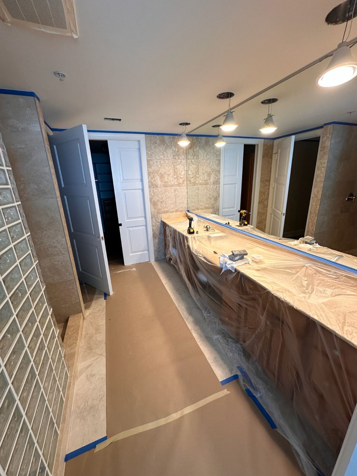 Bathroom undergoing renovation, covered counter, tile walls, open doors, work lights.