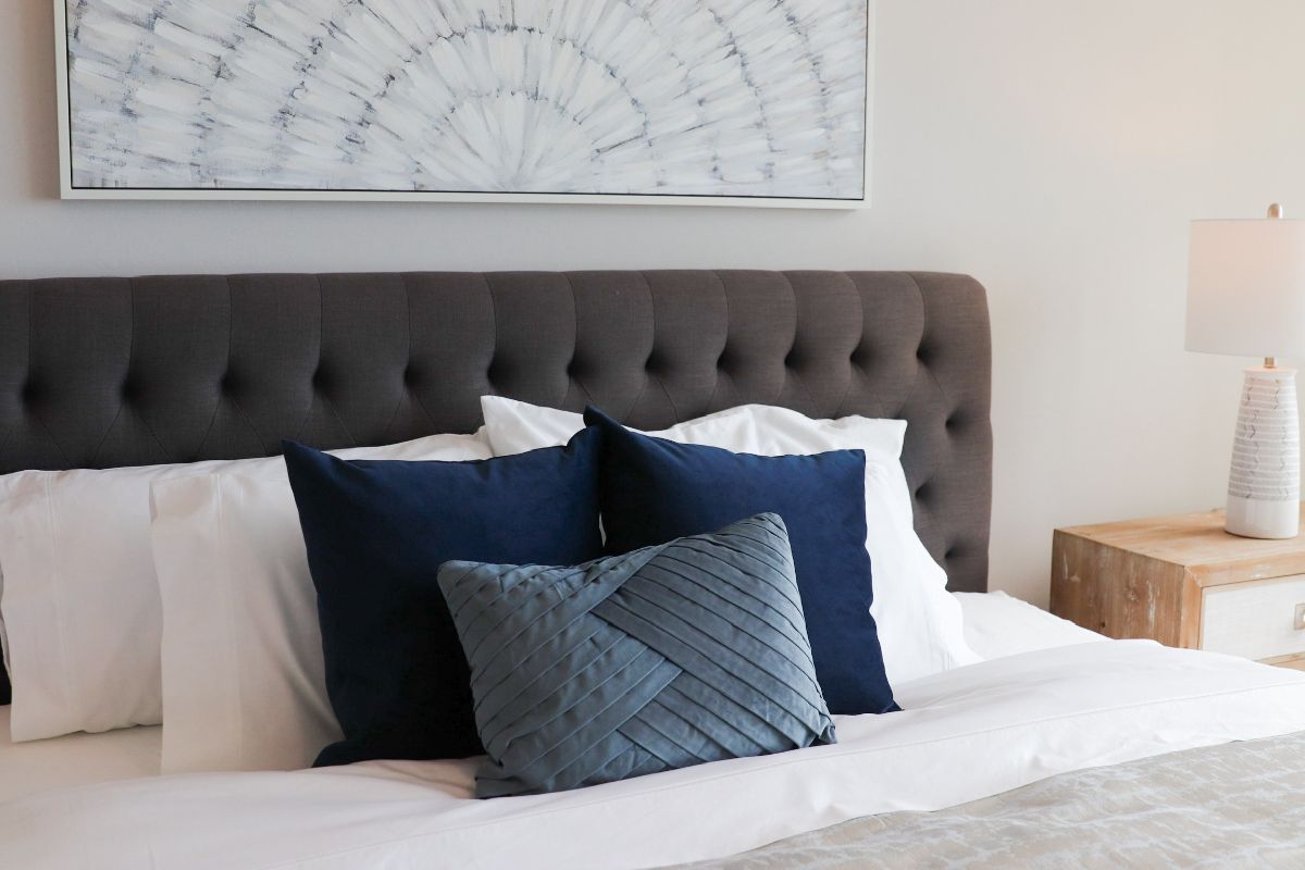 Bedroom with gray tufted headboard, white bedding, navy pillows, and a geometric art piece.