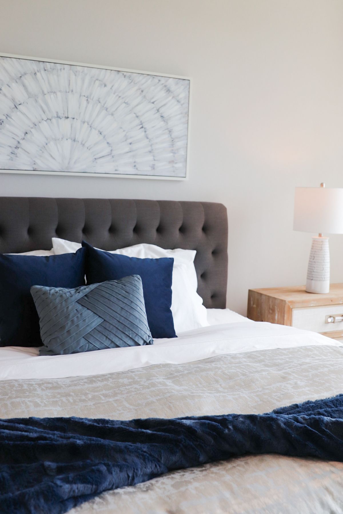 Bedroom with gray tufted headboard, white bedding, navy blue pillows, and a decorative blanket.