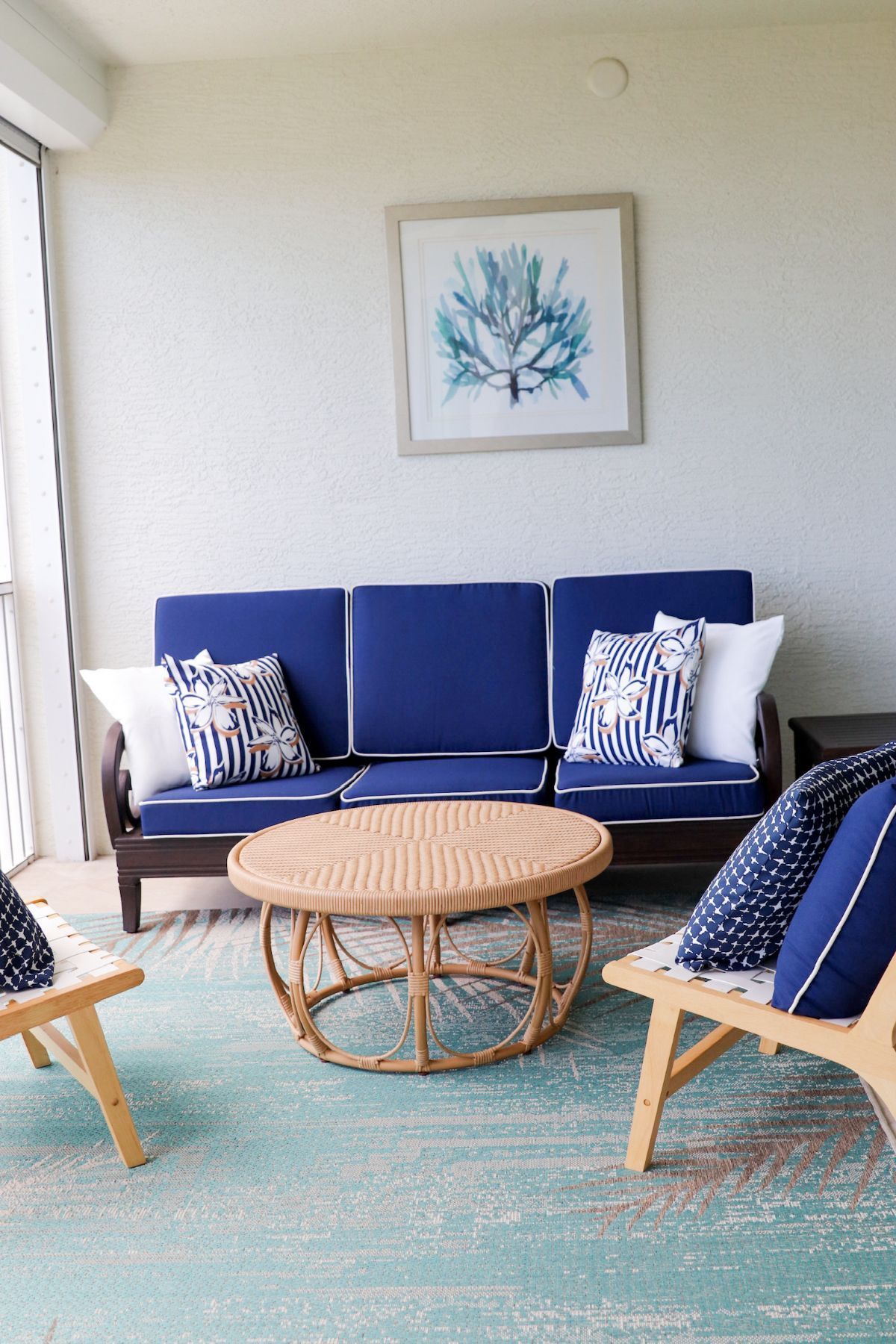 Coastal-themed patio. Blue sofa, chairs, and rug. Rattan coffee table. Artwork of blue coral.