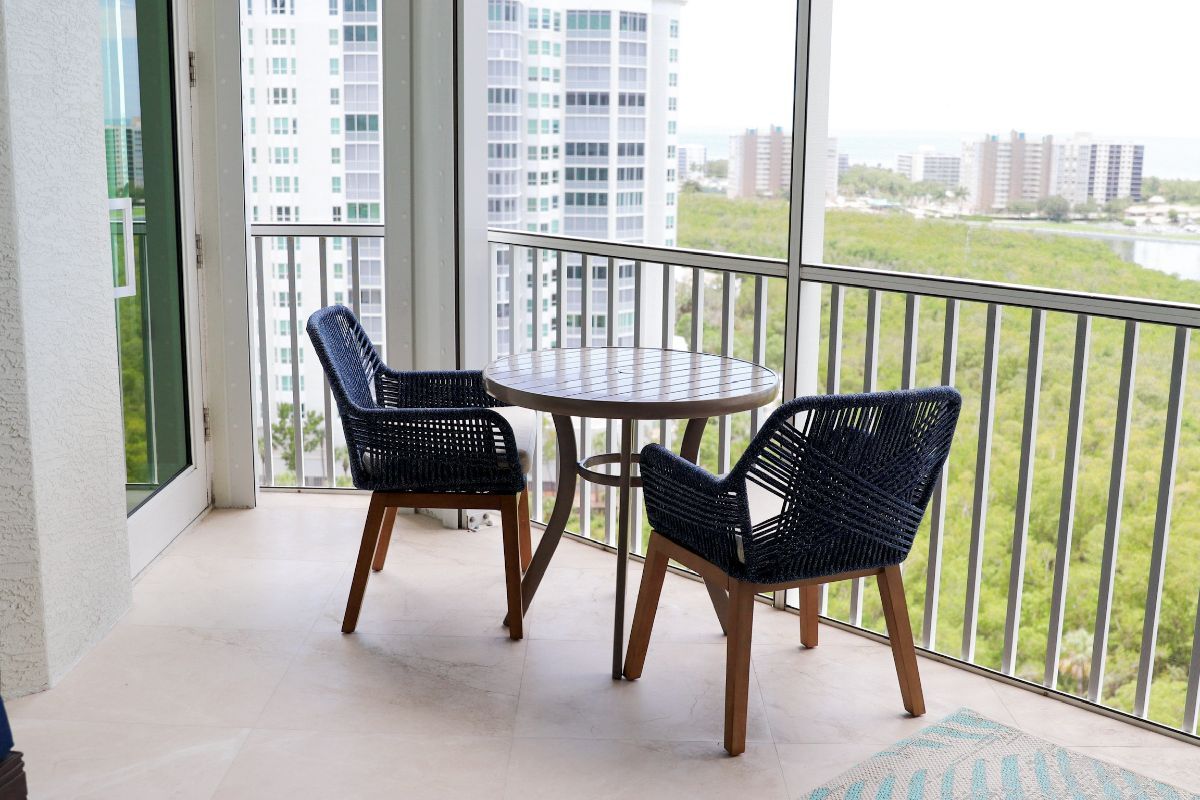 Balcony with two blue woven chairs, a small table, and a view of buildings and greenery.