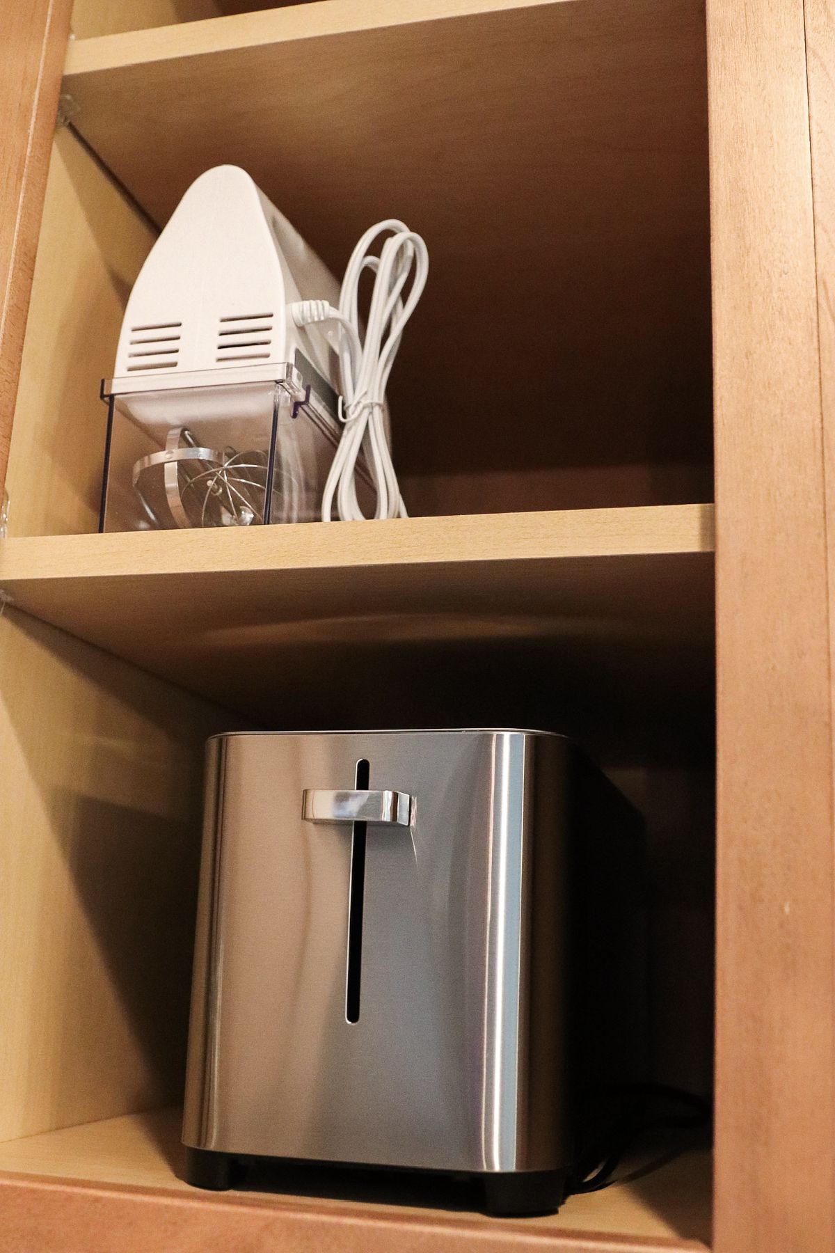 Stainless steel toaster and a white stand mixer inside a wooden kitchen cabinet.