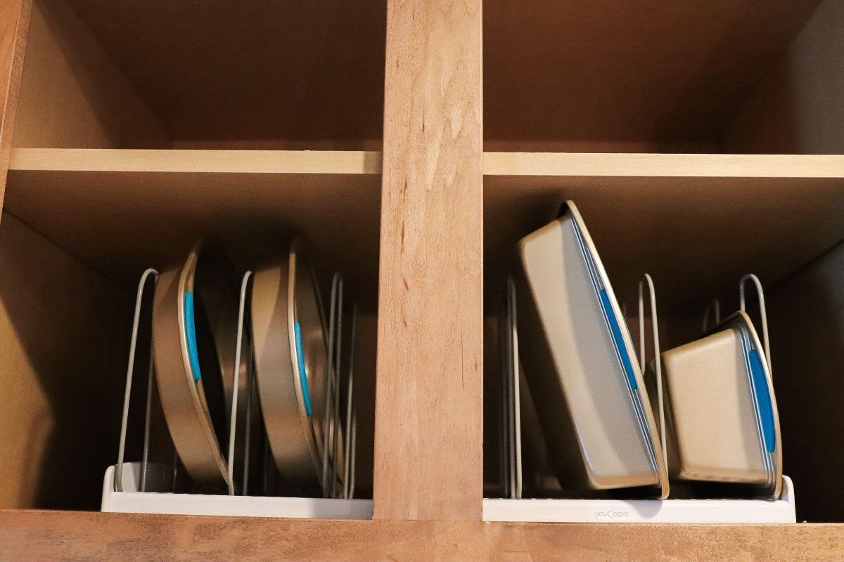 Baking pans stored vertically in a cabinet using dividers. Wooden shelves and cabinet interior.