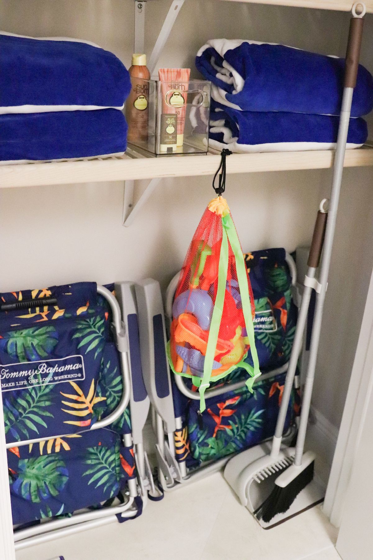 Closet with beach chairs, towels, toys, and cleaning supplies. Blue, green, white, and brown items.