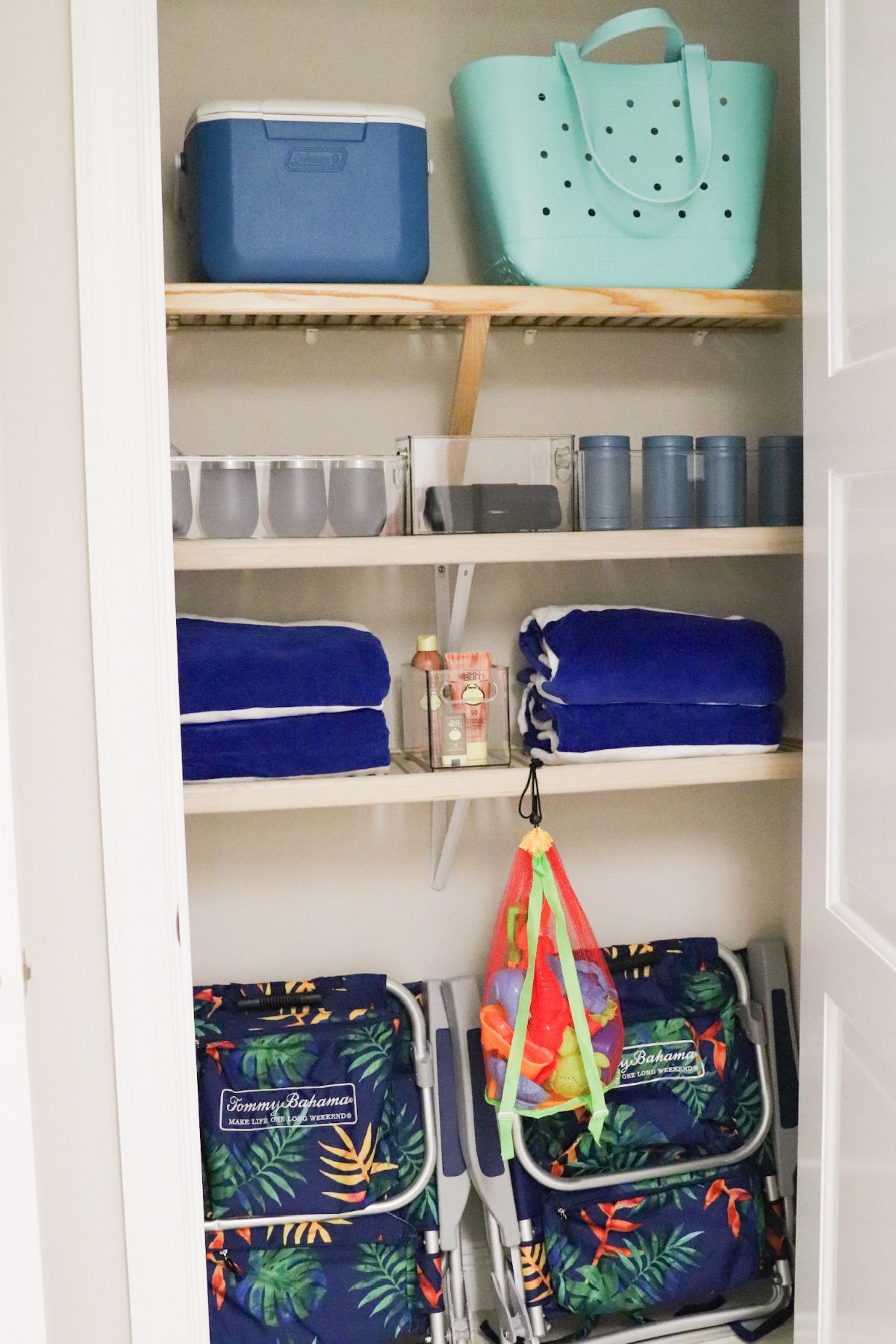 Closet organized with shelves; items include a cooler, tote bag, cups, towels, and beach chairs.