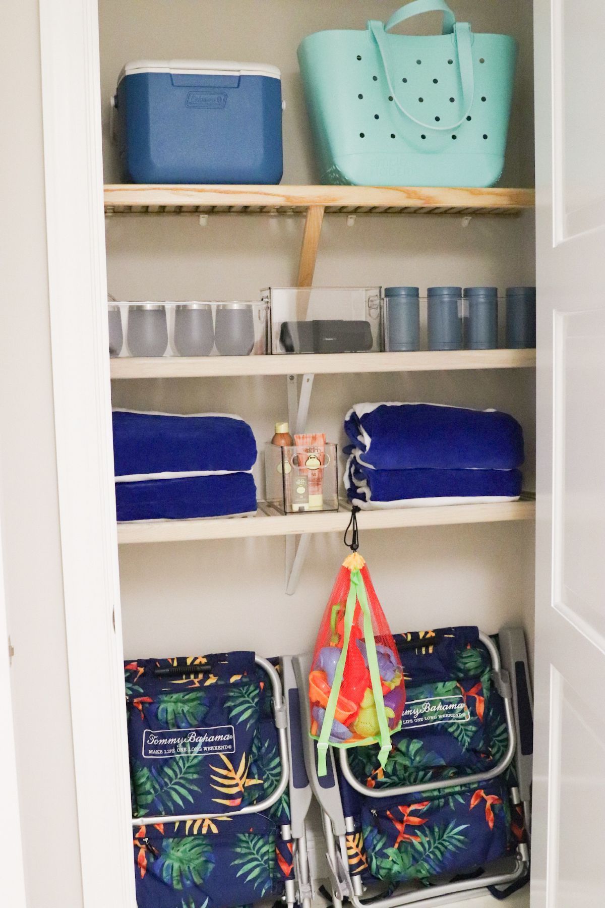 Closet with beach supplies: cooler, tote bag, towels, drinkware, beach chairs, organized on shelves.
