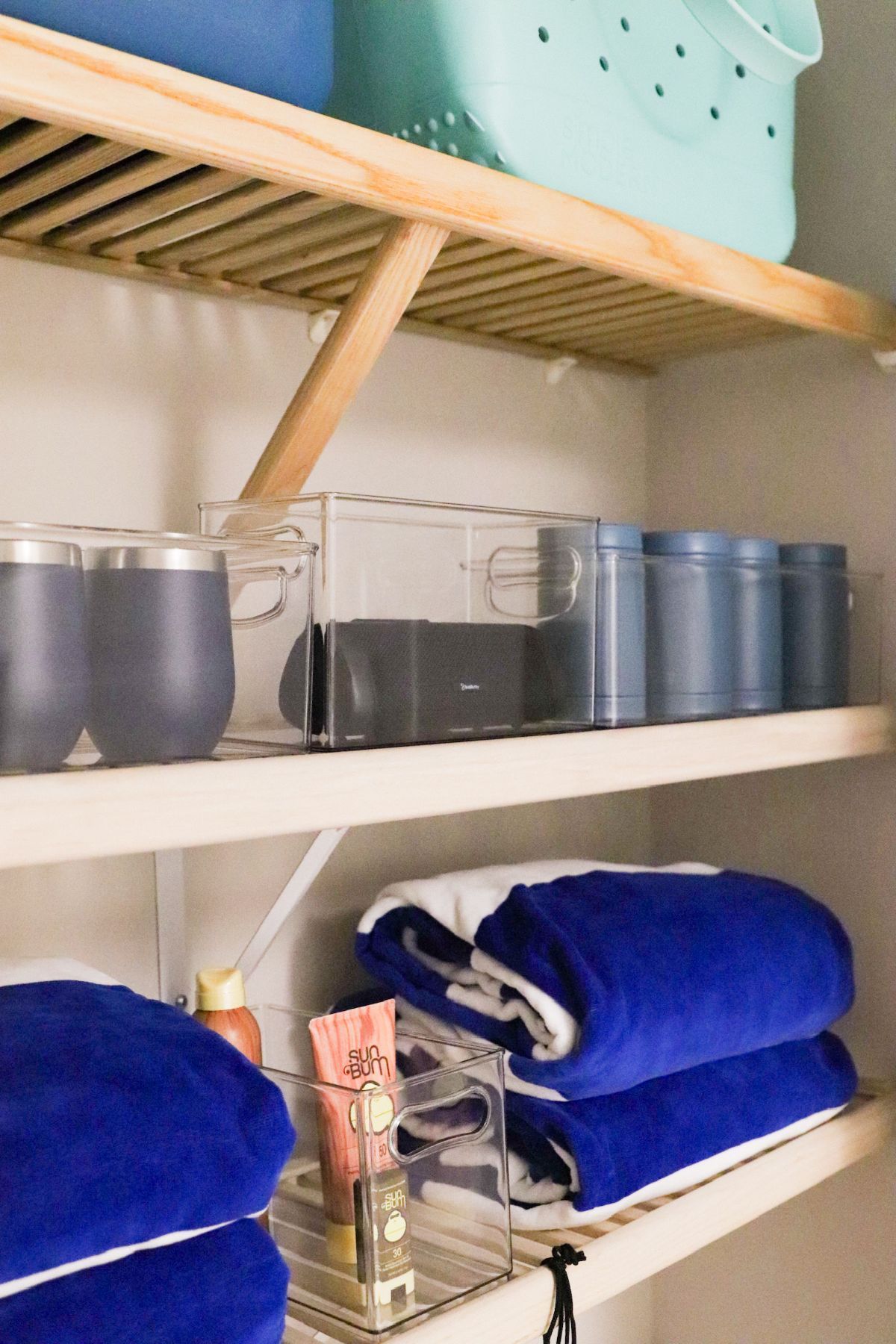 Closet with shelves holding blue towels, containers, and a light teal tote.