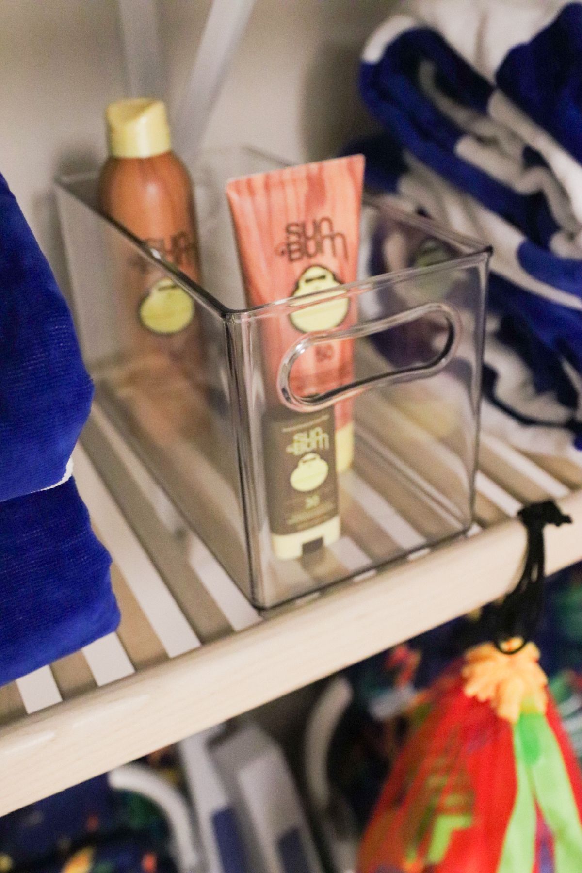 Clear bin holding Sun Bum sunscreen and tanning lotion on a shelf.