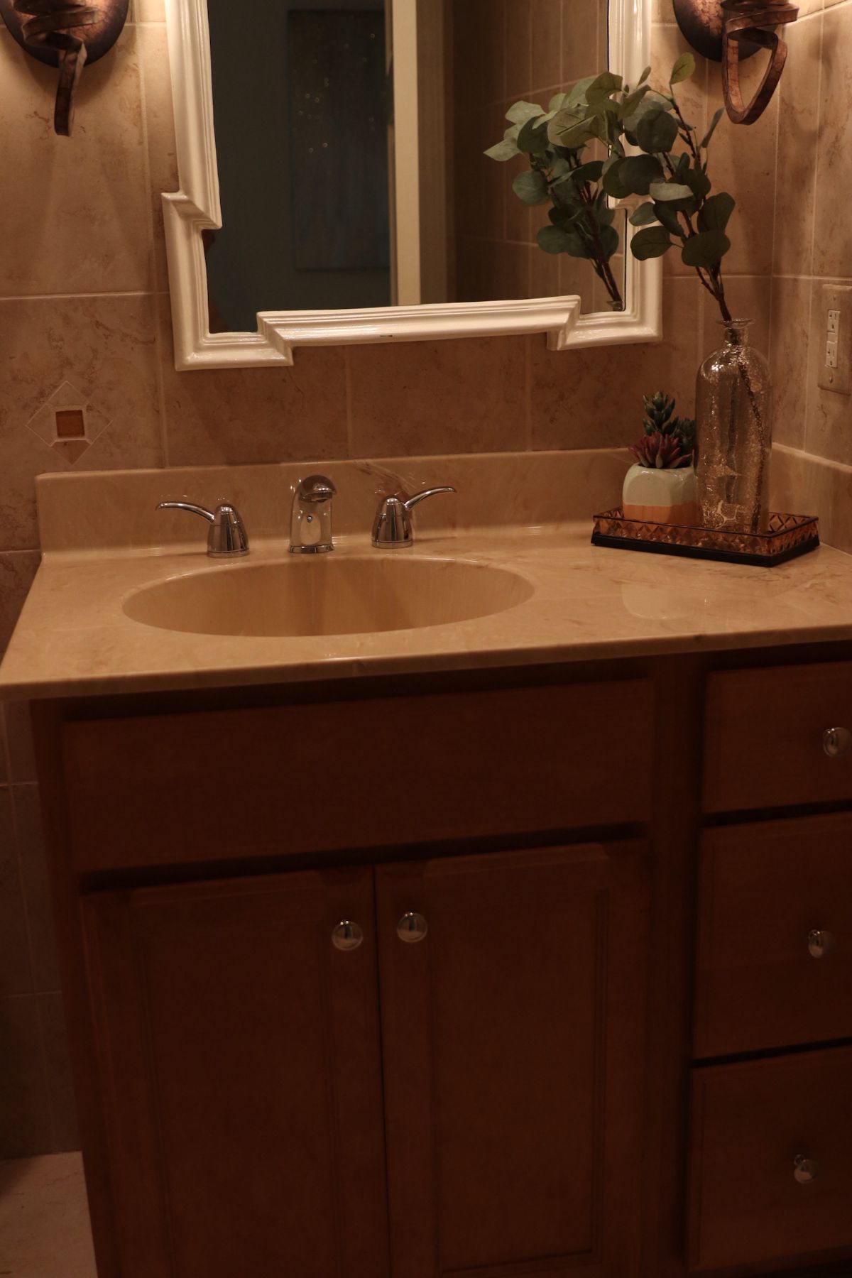 Bathroom vanity with a round sink, wooden cabinets, and a decorative mirror.