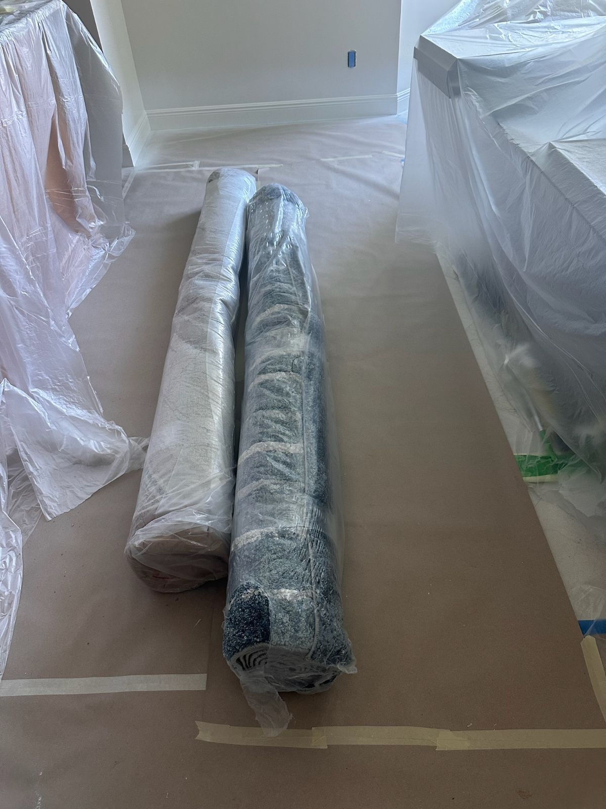 Two rolled rugs wrapped in plastic on a protected floor.