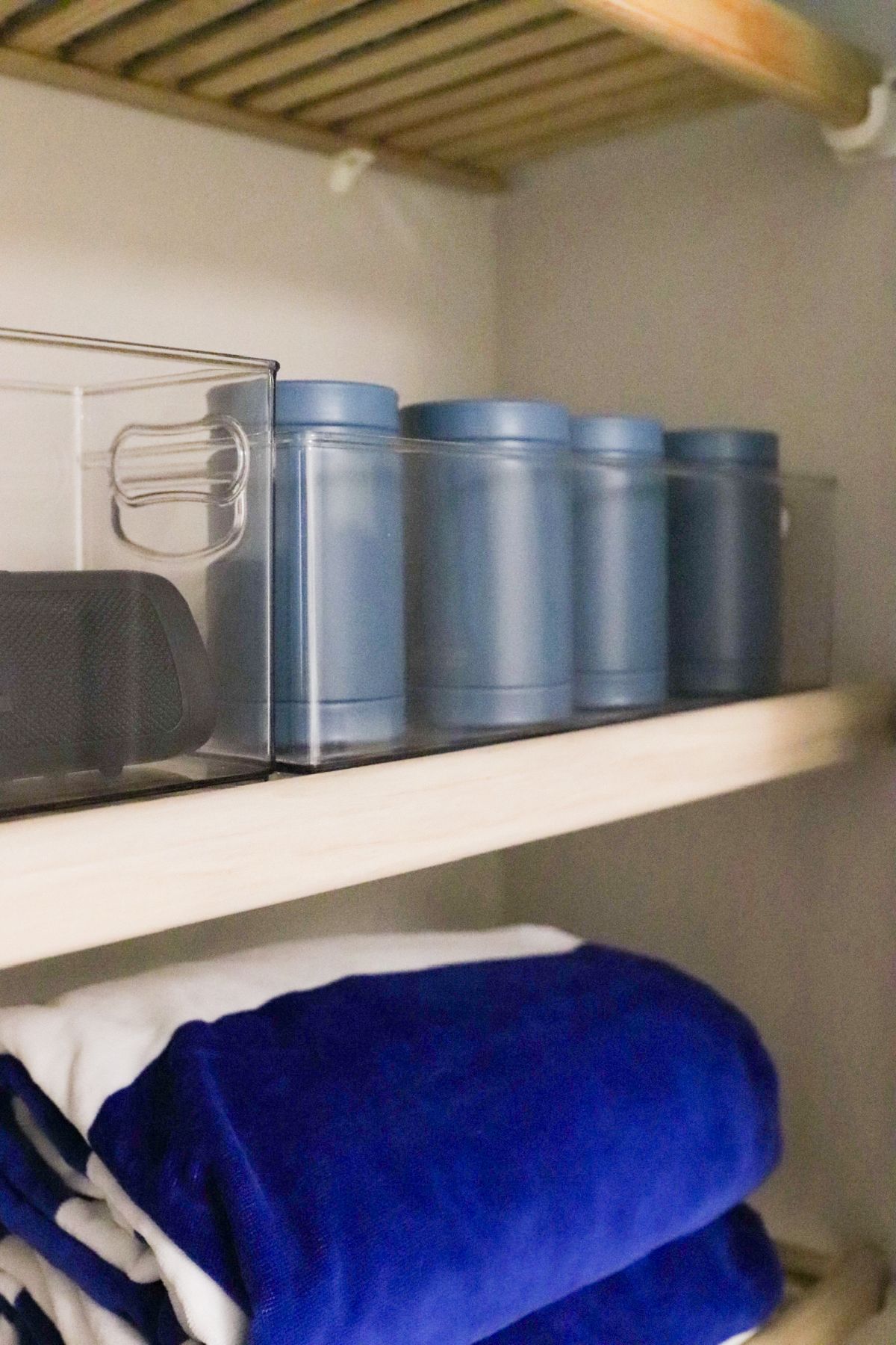 Closet shelf with folded blue towels and blue cylindrical containers.