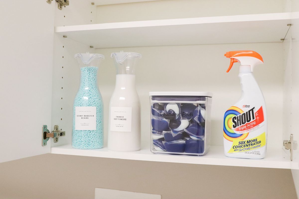 White cabinet shelf with cleaning supplies: laundry beads, spray bottle, container of pods, and spray cleaner.