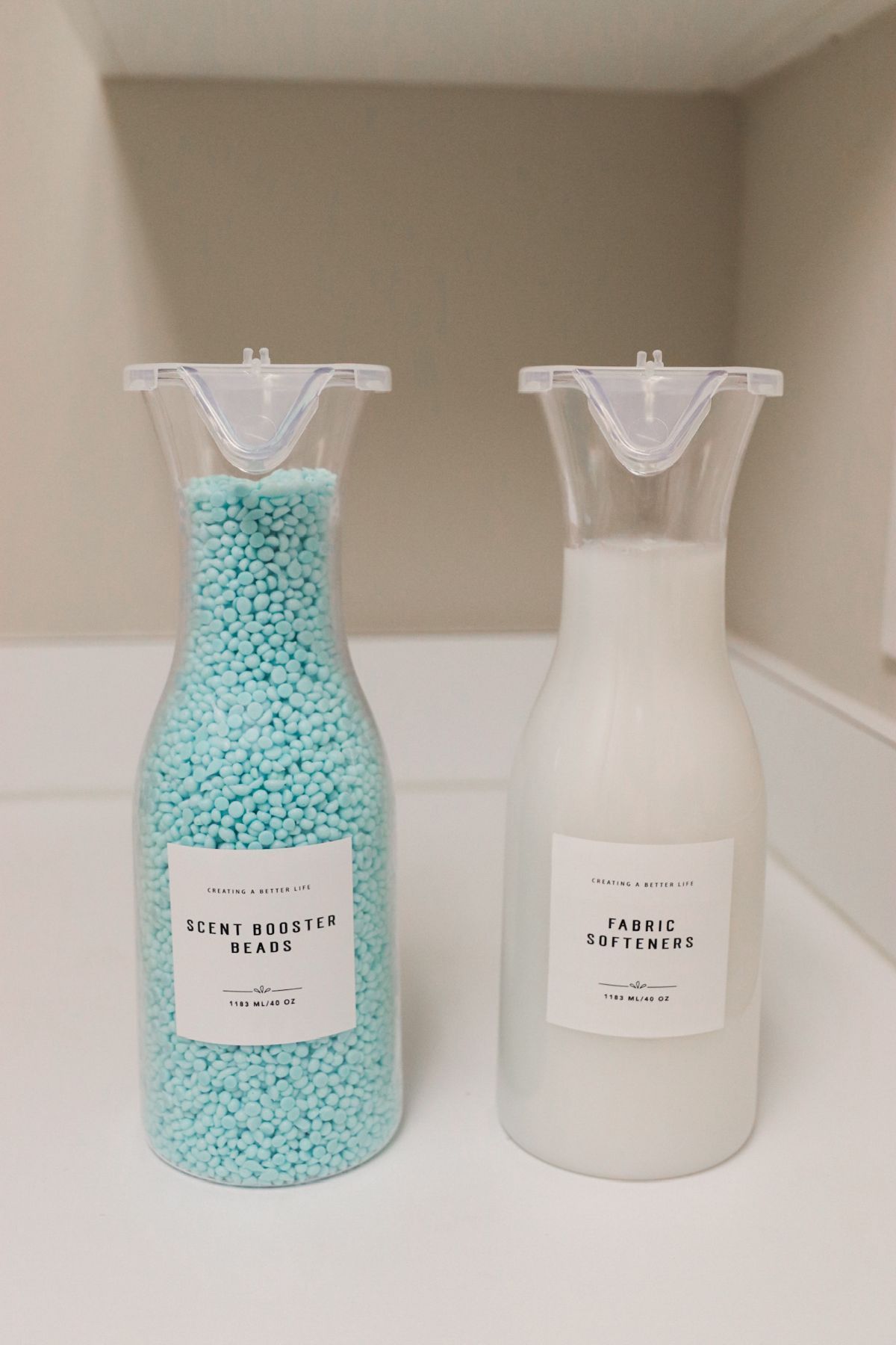 Two clear glass bottles with labels, one containing blue beads, the other white liquid, on a white surface.