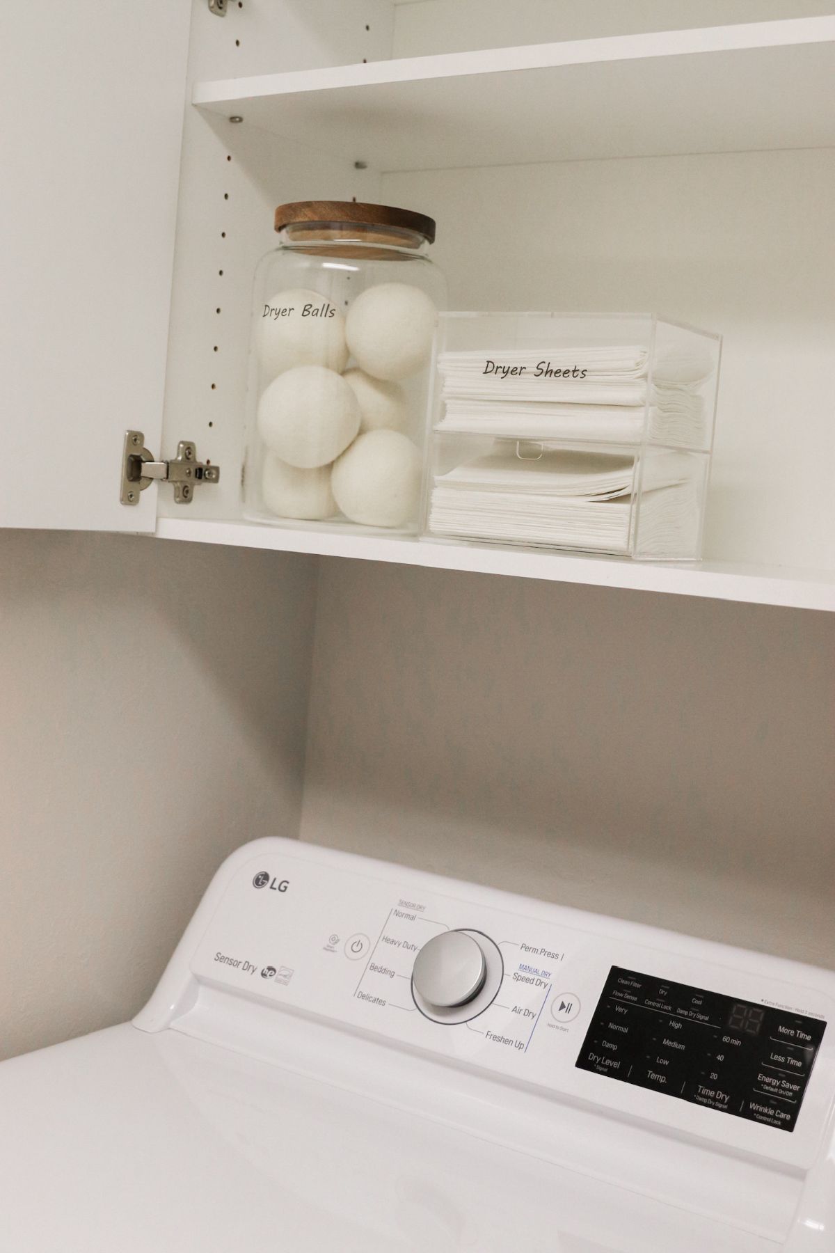 Laundry room cabinet with jar of dryer balls and box of dryer sheets above a washing machine.