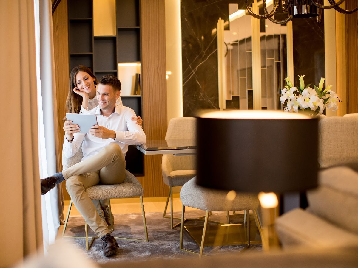 Couple looking at tablet in a modern living room. Woman leans on man's shoulder. Elegant decor, soft lighting.