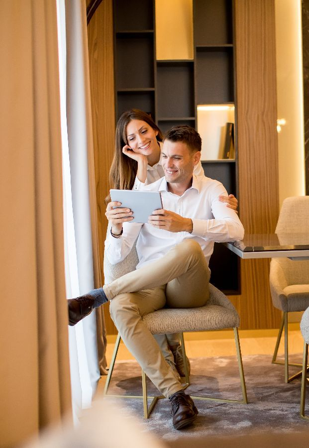 Couple looking at tablet in a modern room, woman's arm around man's shoulder.
