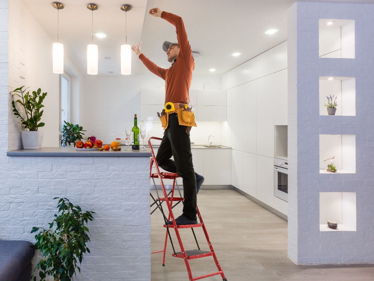 Electrician on a stepladder installing lights in a modern kitchen.