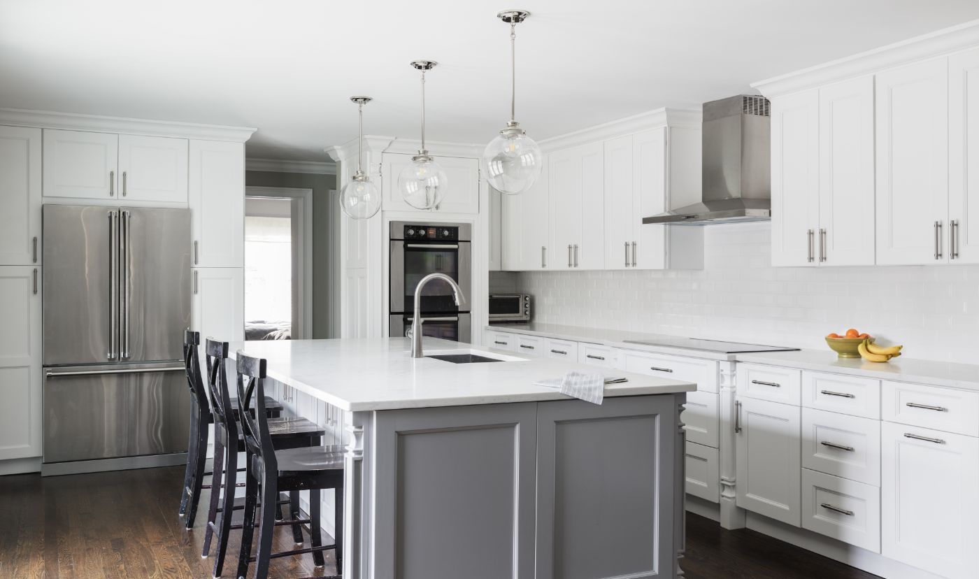 Modern white kitchen with gray island, stainless steel appliances, and dark stools.