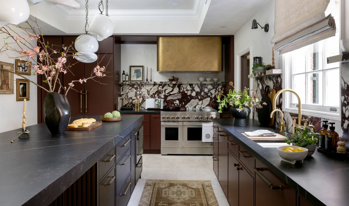 Elegant kitchen with dark cabinets, marble backsplash, gold range hood, and black countertops.