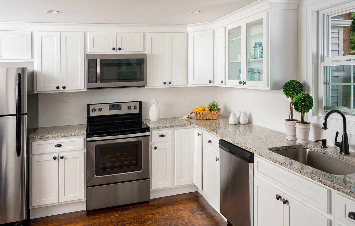 White kitchen with stainless steel appliances, granite countertops, and wooden floors.