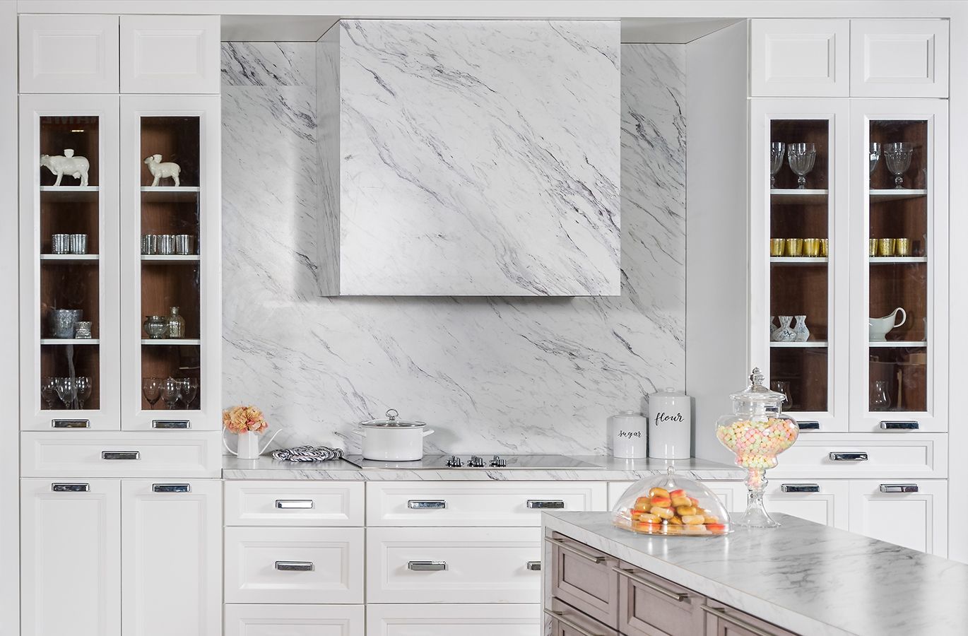 White kitchen with marble backsplash, cabinets, and island. Range hood centered over cooktop.