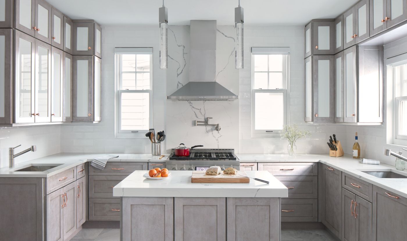 A modern kitchen with grey cabinets, white countertops, and stainless steel range hood.