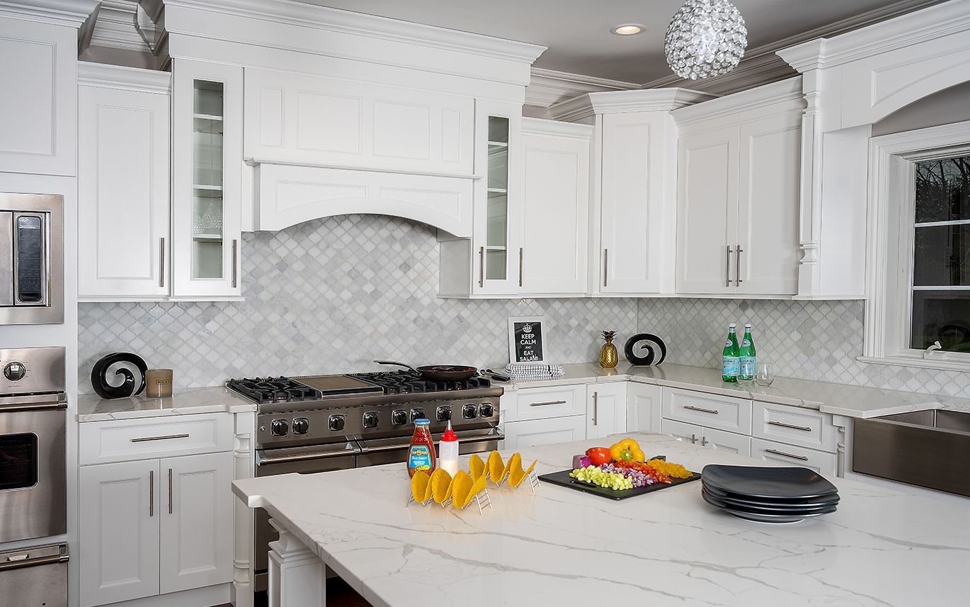 White kitchen with stainless steel appliances, marble backsplash, and island with food.