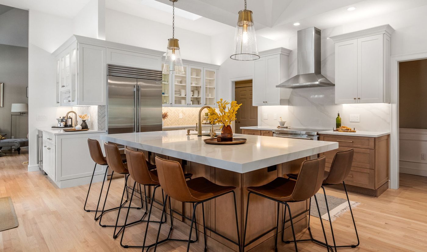 Modern kitchen with island, brown leather bar stools, white cabinets, and stainless steel appliances.