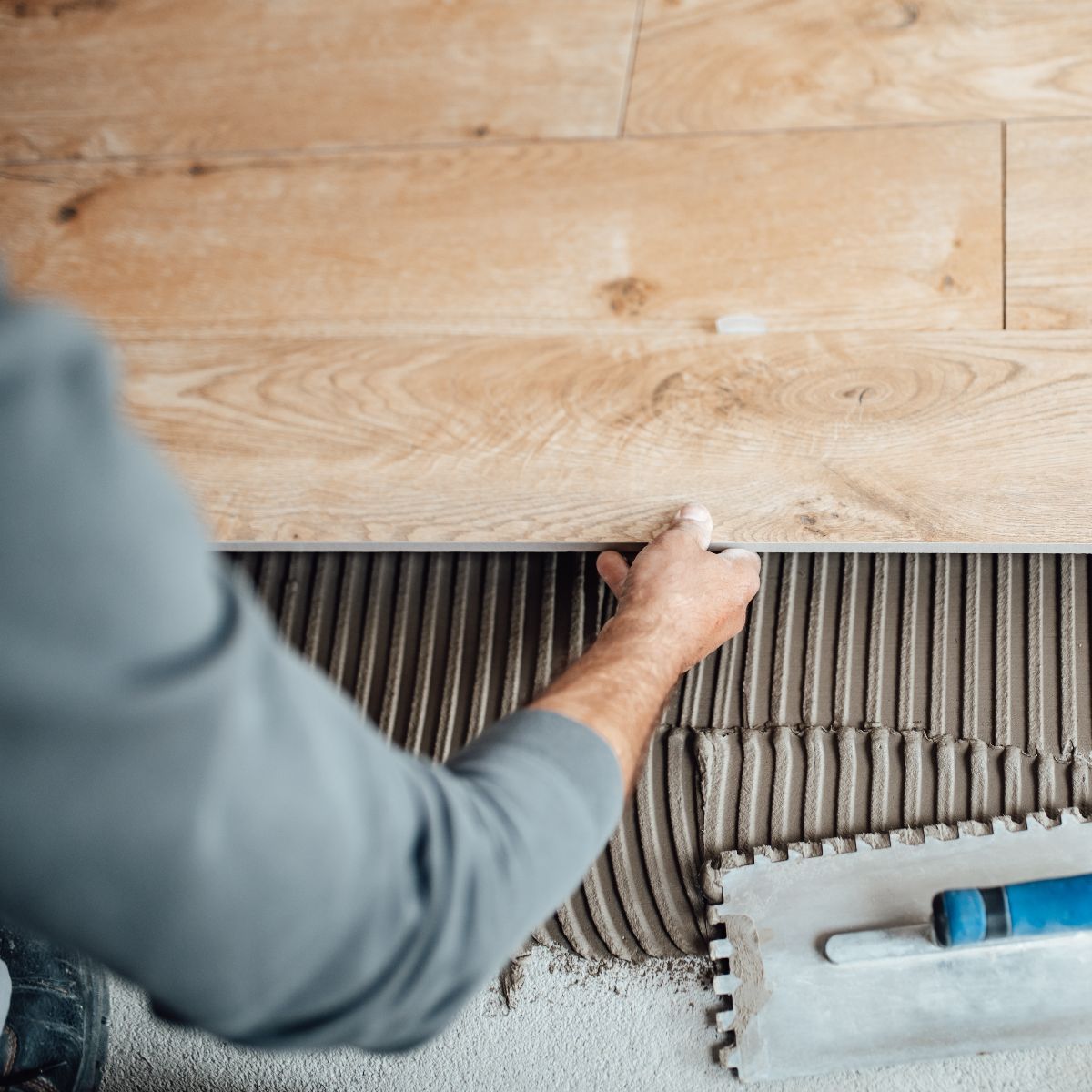 Person installing wood-look tile with a notched trowel and adhesive.