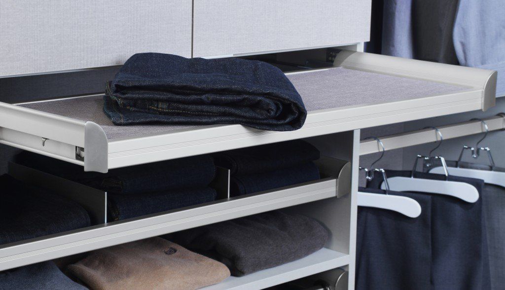 Closet with pull-out shelf holding folded blue sweater. More folded clothes are stacked below.
