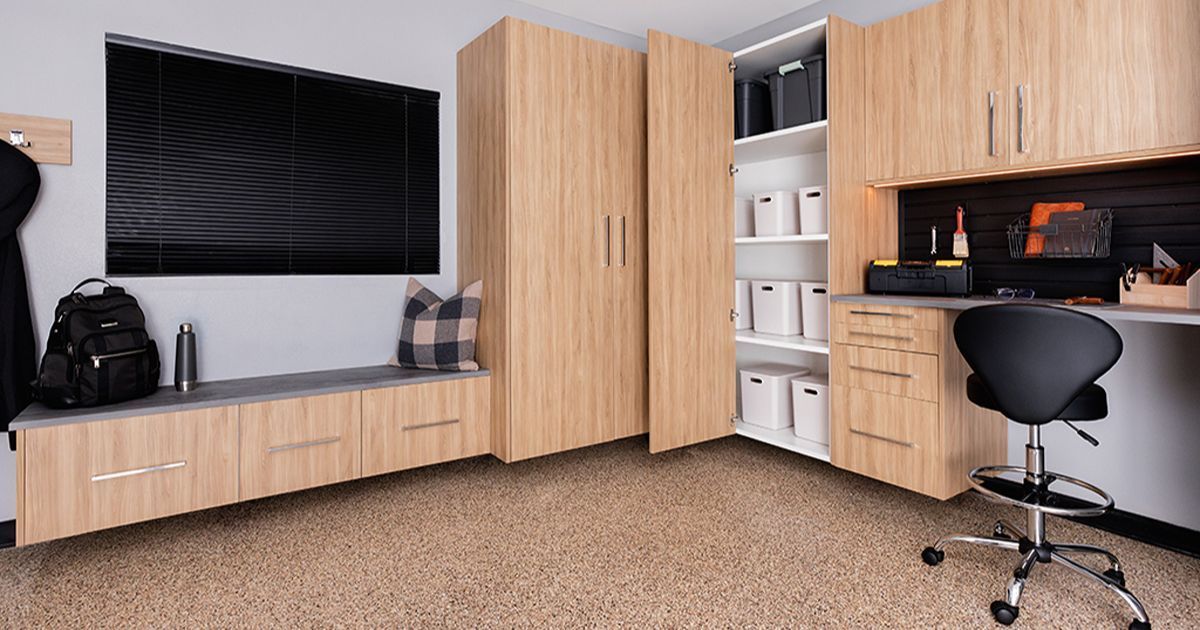 Garage with light wood cabinets, storage bench, desk, and office chair.
