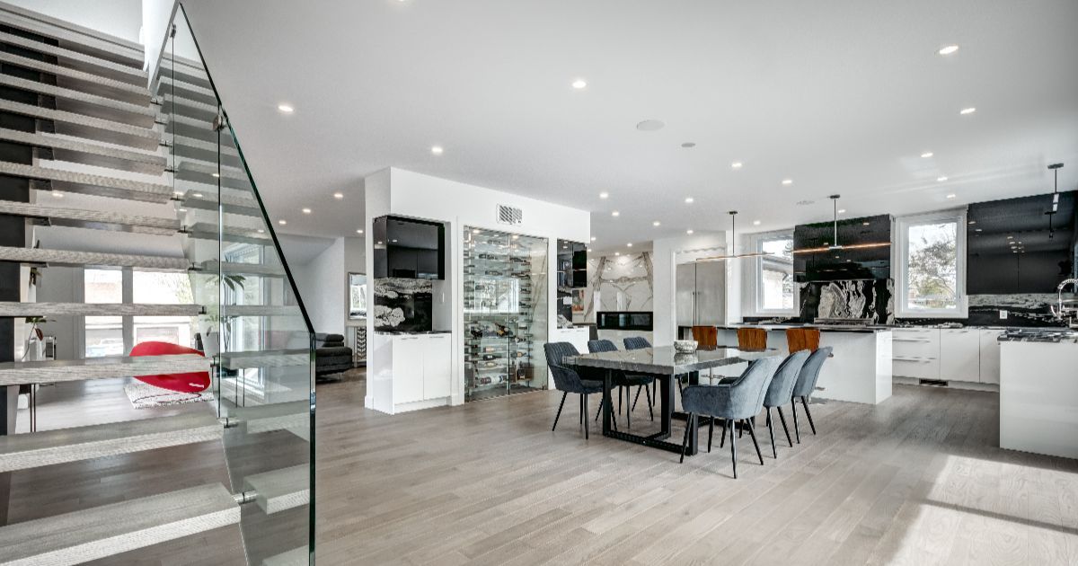 Modern open-concept living space with staircase, kitchen, and dining area. Light wood floors and white cabinetry.