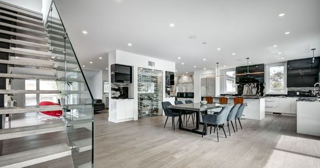 Modern open-concept living space with staircase, kitchen, and dining area. Light wood floors and white cabinetry.