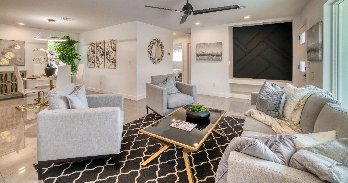 Living room with gray furniture, black patterned rug, black coffee table, artwork, and ceiling fan.