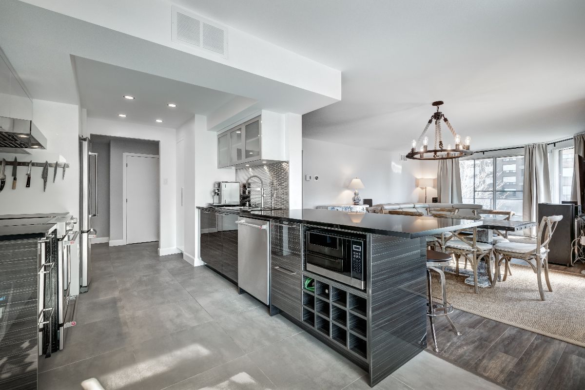 Modern kitchen with stainless steel appliances, open to dining area with chandelier.