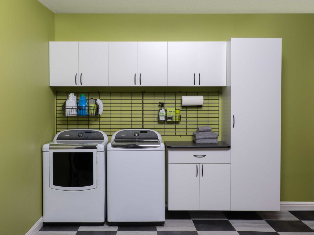 Laundry room with white appliances, cabinets, and black/white checkered floor. Green wall.