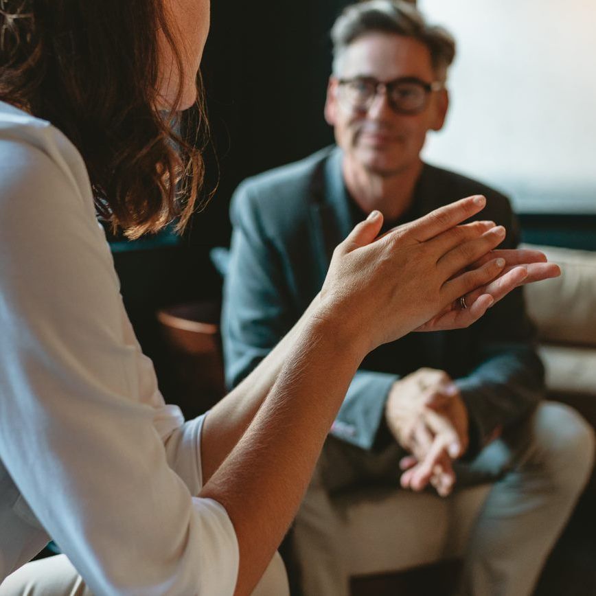 A man and a woman are sitting on a couch talking to each other