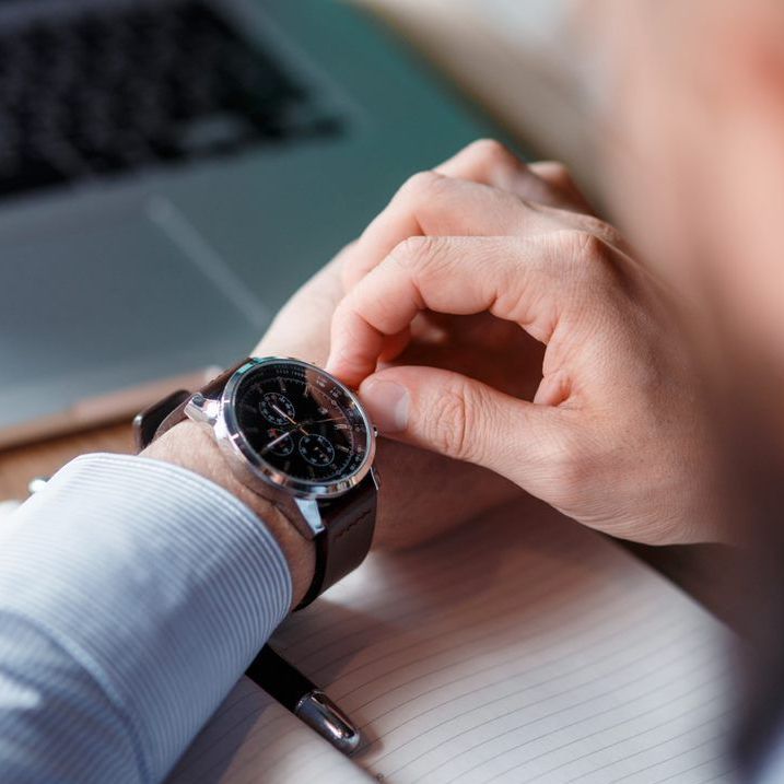 A man is looking at his watch while sitting at a desk