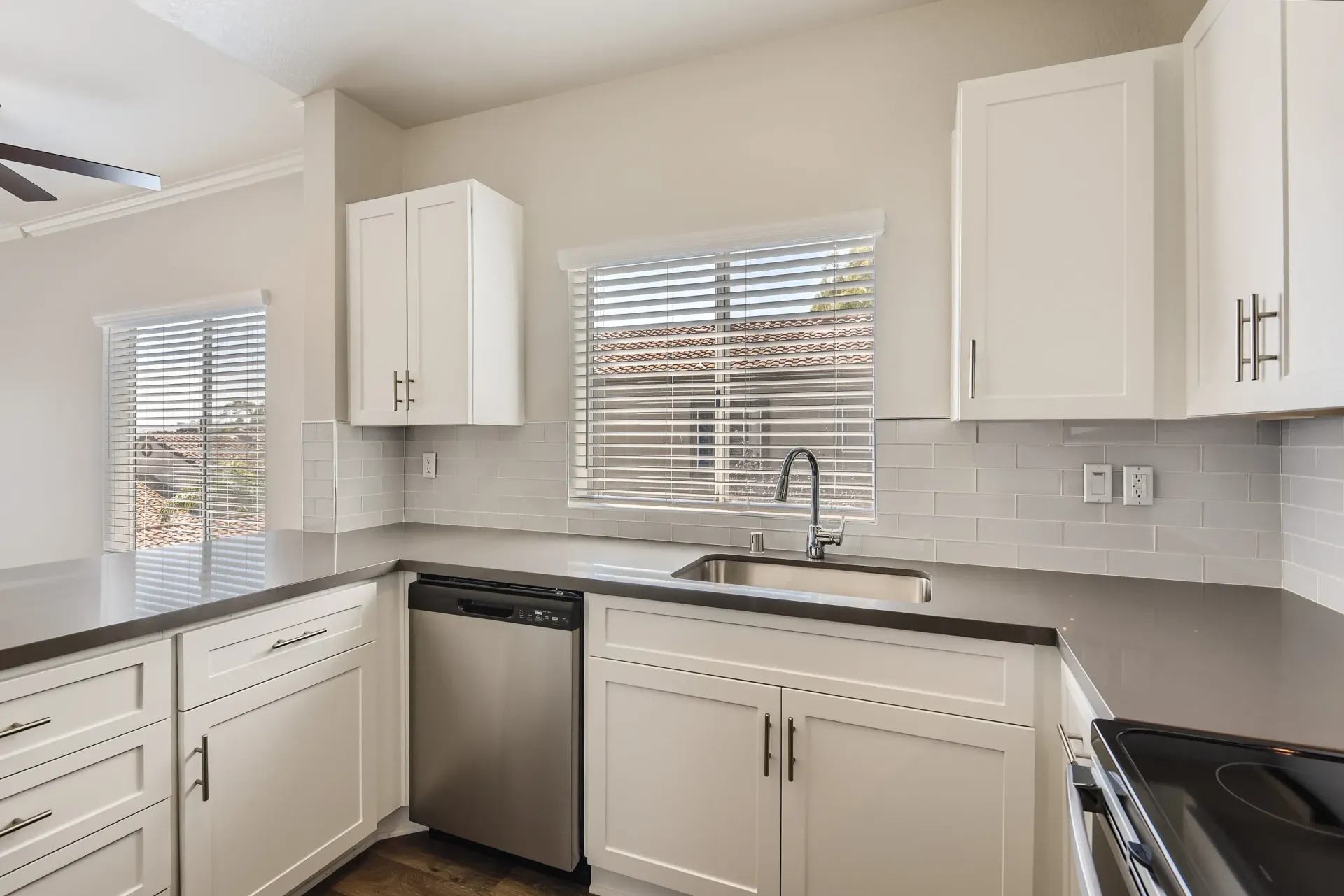 Bright kitchen with white cabinets, gray countertops, and stainless steel sink.
