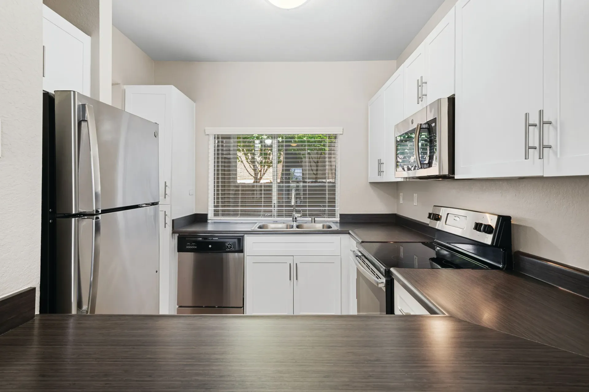 Modern apartment kitchen with white cabinets, stainless steel appliances, and a window above the sink.