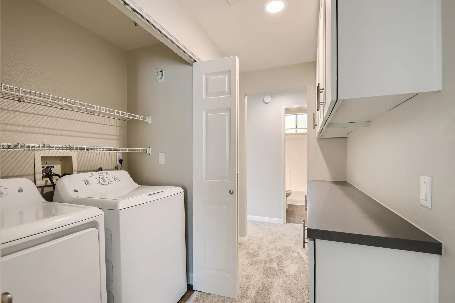In-unit laundry closet with a washer and dryer, white wire shelving, and a folding counter.