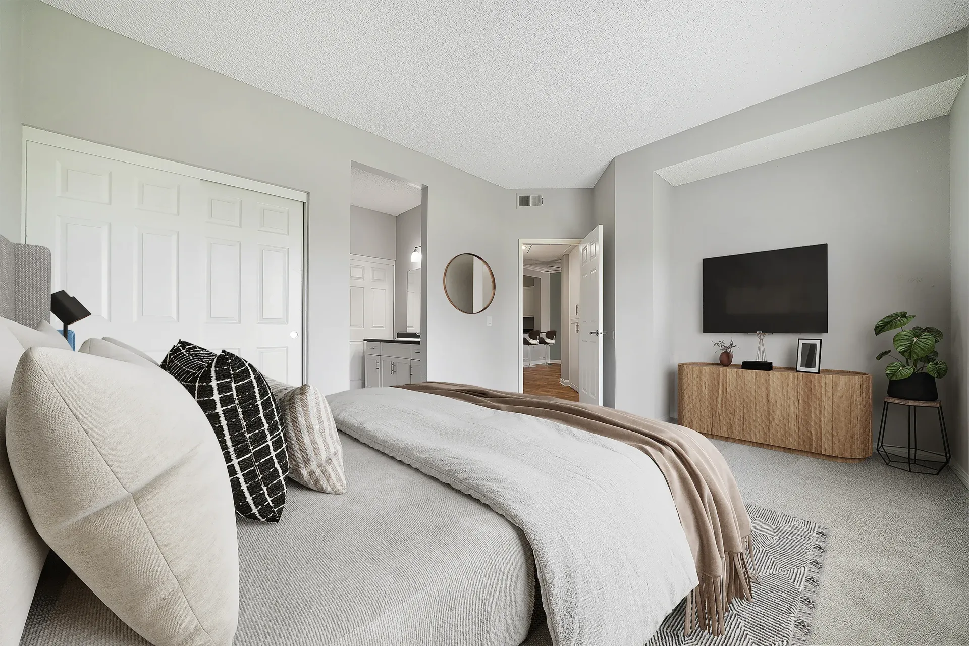 Modern apartment bedroom with a large bed, wall-mounted TV, and a wooden dresser.