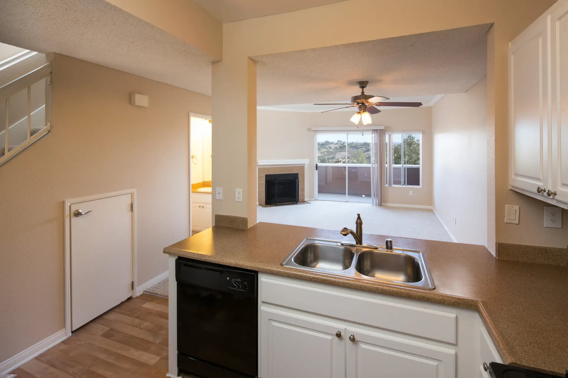 Open kitchen with double sink, dishwasher, and view into living room with fireplace and sliding balcony door.