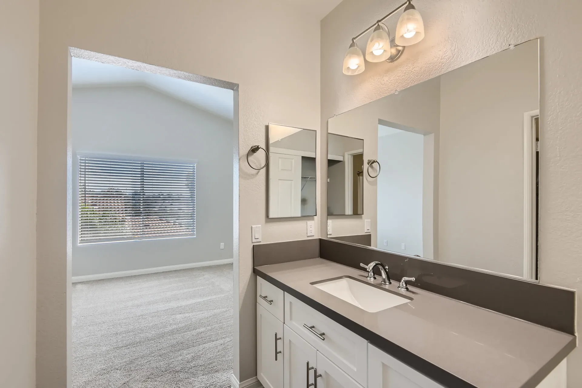 Bathroom vanity with sink, mirrors, and overhead light; doorway to living area.