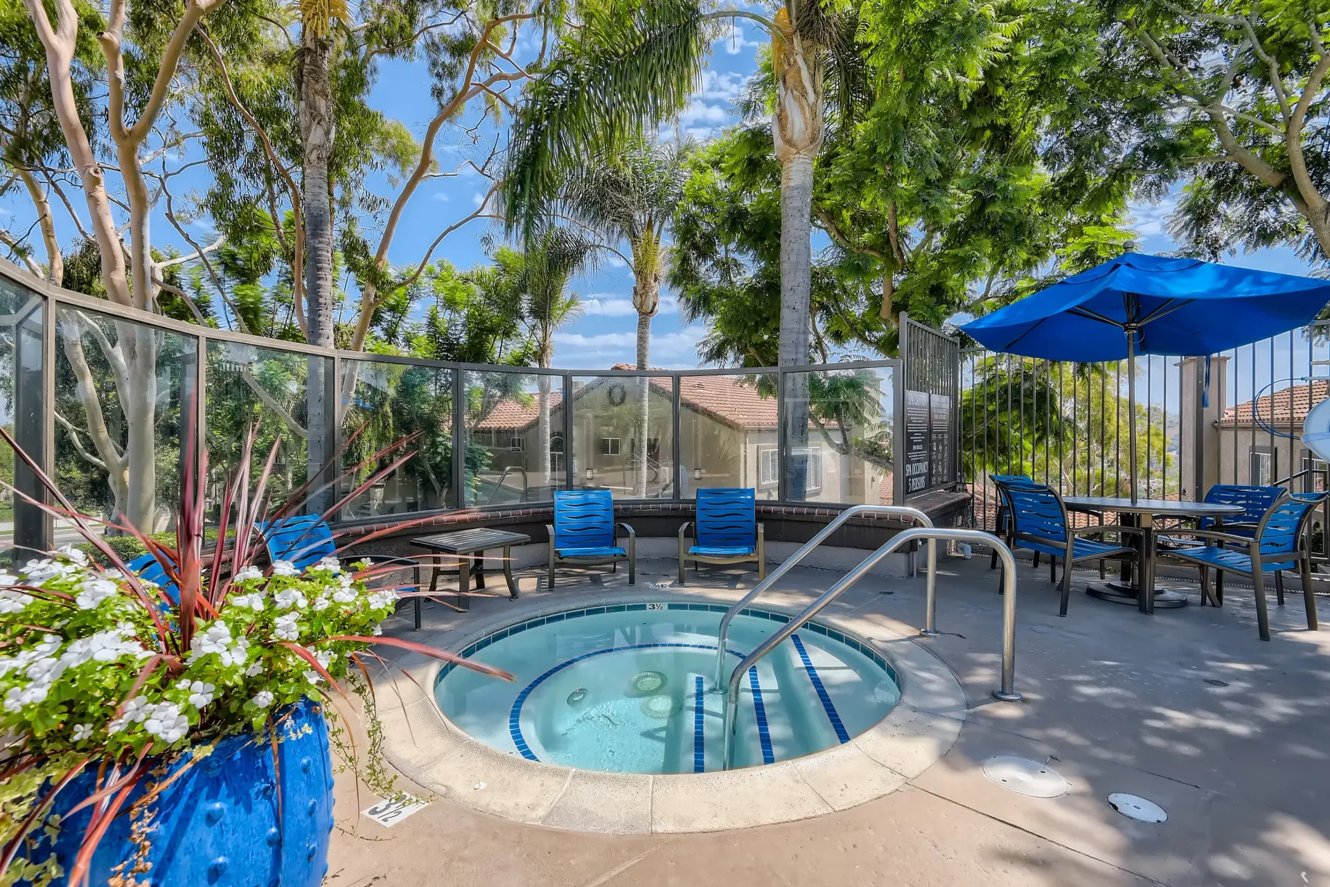 Outdoor community pool with hot tub, blue lounge chairs, and shaded seating under a blue umbrella.