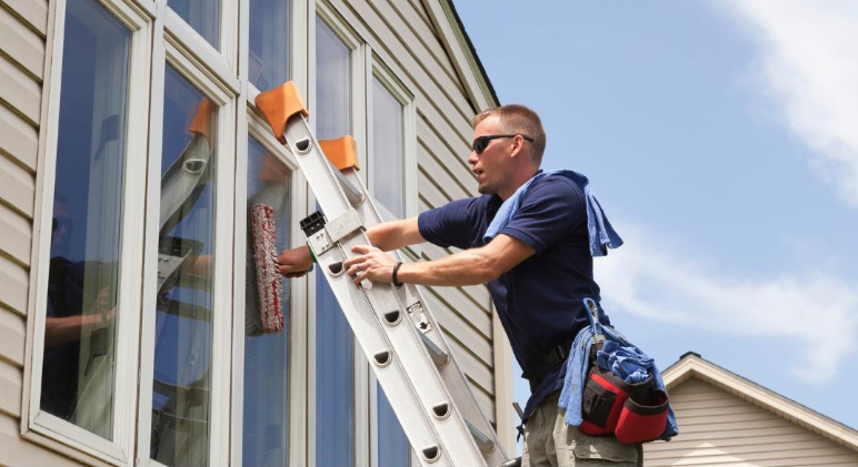 A man is standing on a ladder cleaning a window.